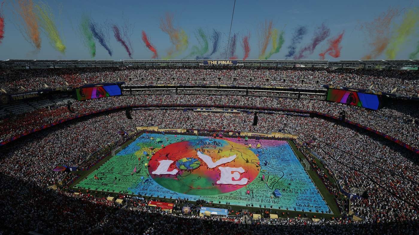 Packed stadium during a final; a huge multicolored artwork covers the field with fans in the stands. Packed stadium during a final; a huge multicolored artwork covers the field with fans in the stands.