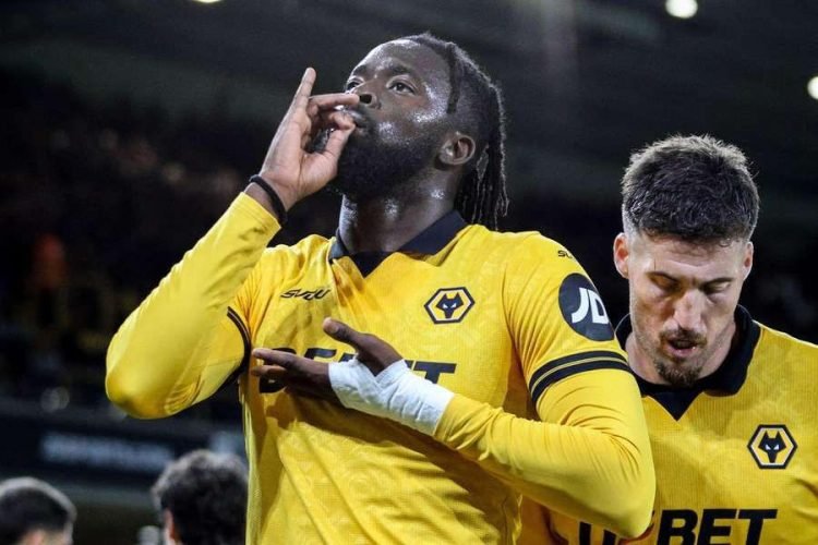 Wolverhampton players in yellow jerseys celebrate on the pitch; foreground player makes a shushing gesture with his fingers by his mouth.