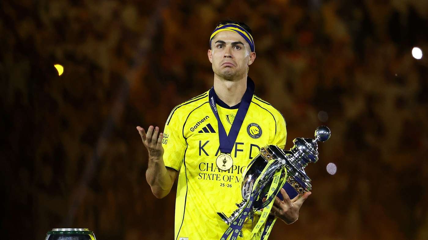 Athlete in a yellow jersey wearing a medal, holding a large silver trophy with ribbons at an award ceremony, looking up thoughtfully. Athlete in a yellow jersey wearing a medal, holding a large silver trophy with ribbons at an award ceremony, looking up thoughtfully.