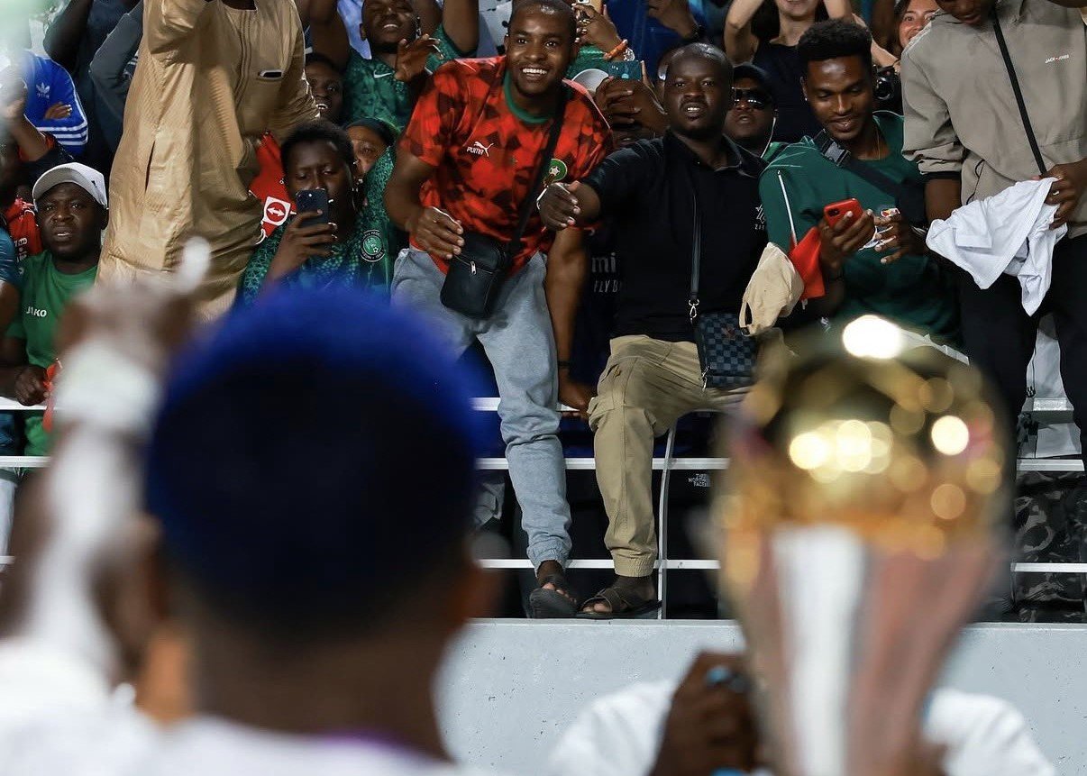Crowd of excited fans behind a barrier, some taking photos, with a large trophy in the foreground blurred. Crowd of excited fans behind a barrier, some taking photos, with a large trophy in the foreground blurred.