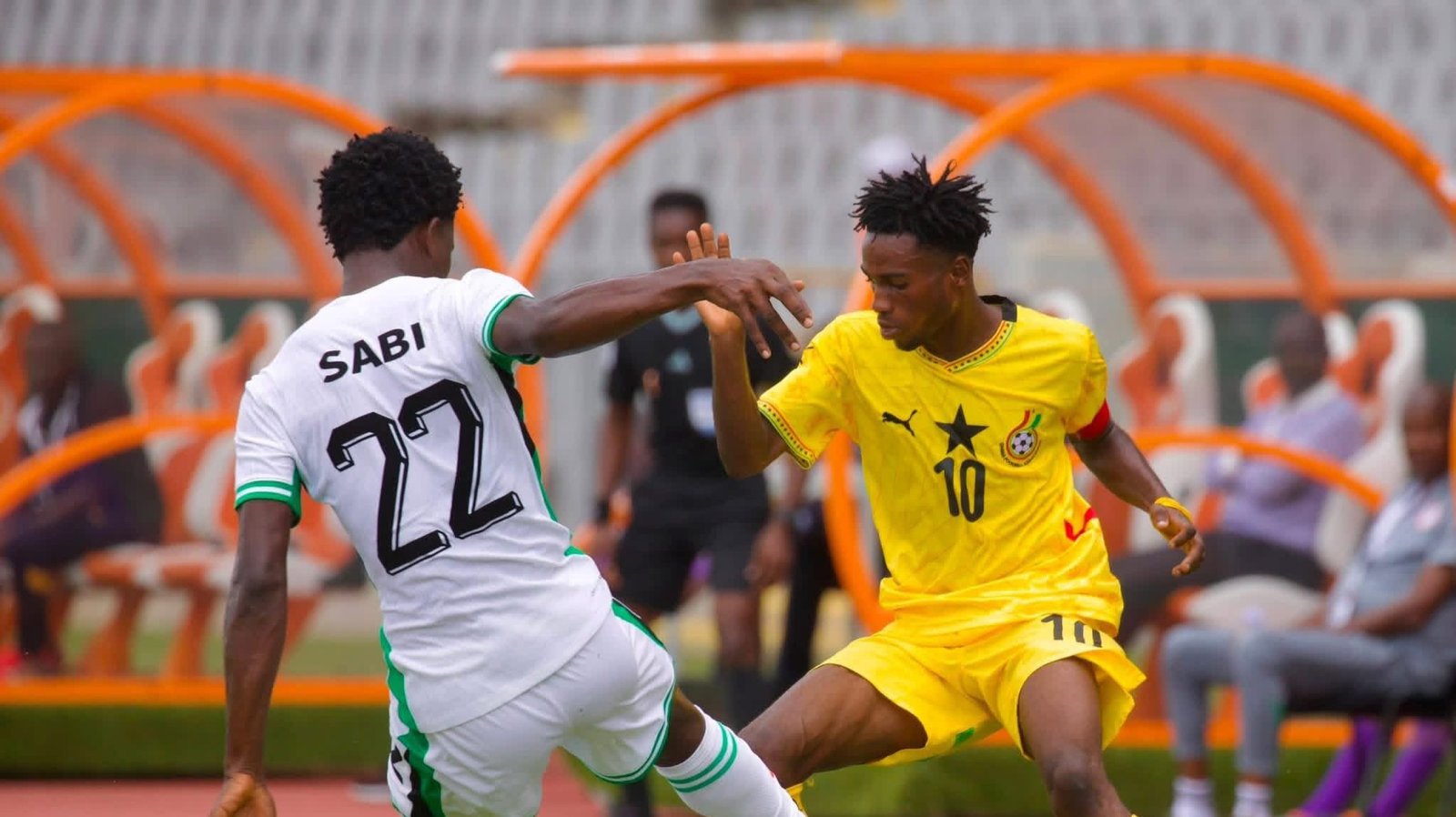 Two soccer players in a duel for the ball during a match: white kit with green trim (#12) against a yellow kit (#10). Two soccer players in a duel for the ball during a match: white kit with green trim (#12) against a yellow kit (#10).