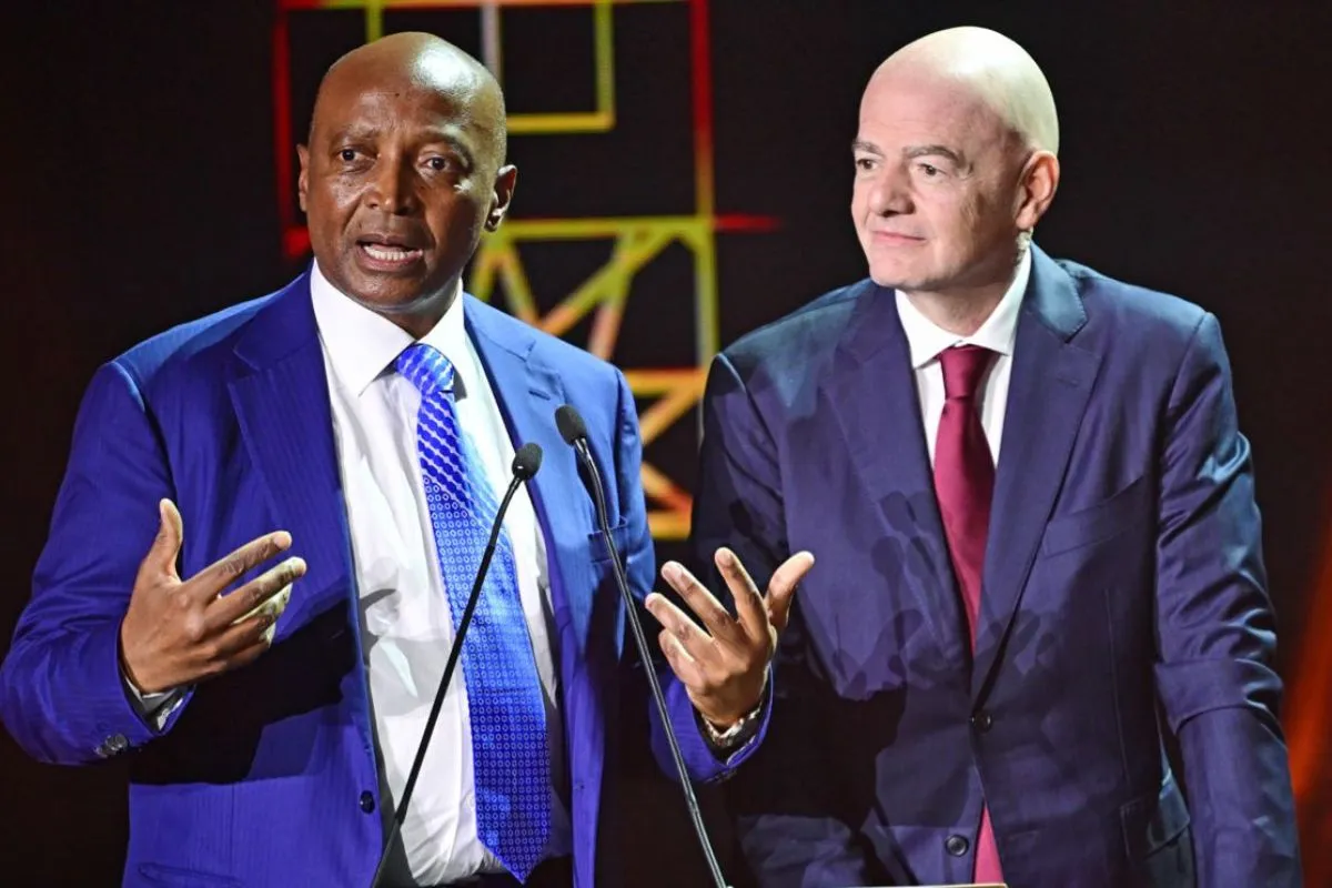 Two men in suits speak at microphones on a stage, one gesturing with his hands.
