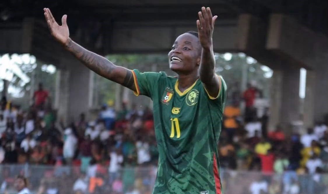 Soccer player in a green jersey with number 11 raises arms in celebration on the field, with a blurred cheering crowd in the background. Soccer player in a green jersey with number 11 raises arms in celebration on the field, with a blurred cheering crowd in the background.