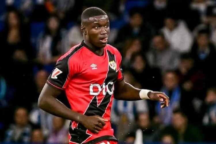 Soccer player in a red and black jersey running on the field during a match, crowd in the stands behind him. Soccer player in a red and black jersey running on the field during a match, crowd in the stands behind him.