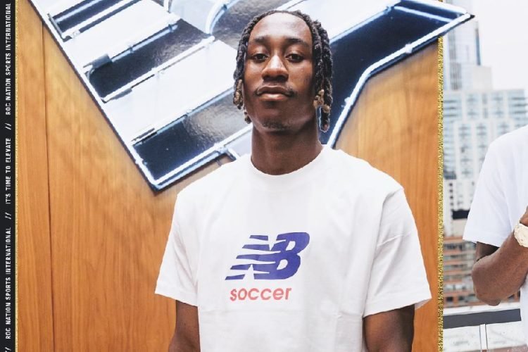 Young man with braided hair wearing a white New Balance soccer shirt, standing in front of a mural with a cityscape in the background. Young man with braided hair wearing a white New Balance soccer shirt, standing in front of a mural with a cityscape in the background.