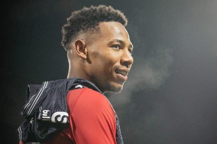 Smiling man in a red athletic top with a dark jacket draped over his shoulders, outdoors at night with foggy air in the background. Smiling man in a red athletic top with a dark jacket draped over his shoulders, outdoors at night with foggy air in the background.