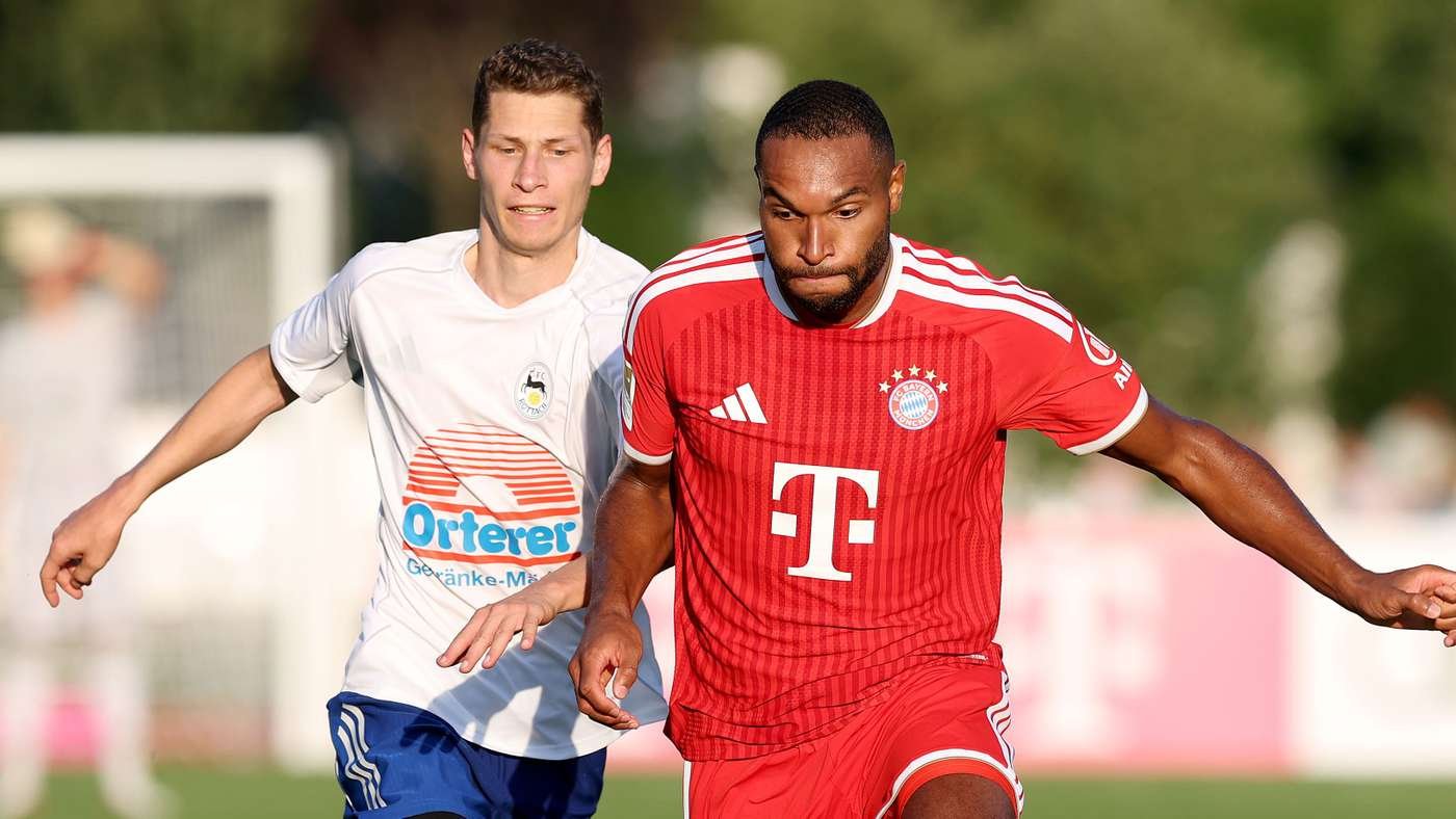 Two male soccer players chase the ball during a match; one wears a red Bayern Munich kit, the other a white kit, on a sunny field. Two male soccer players chase the ball during a match; one wears a red Bayern Munich kit, the other a white kit, on a sunny field.