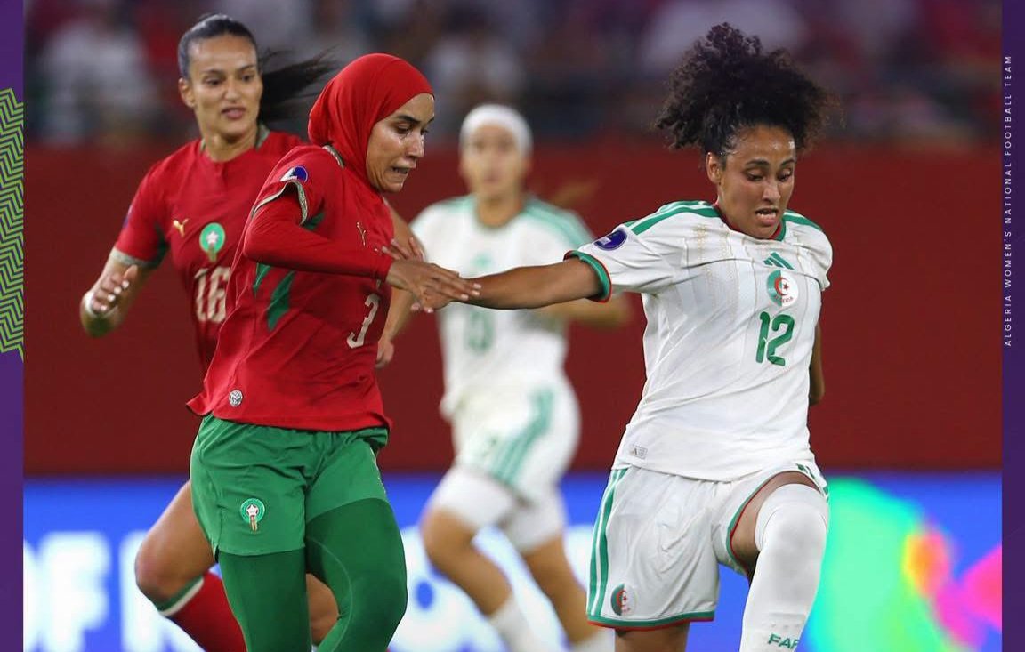 Two female soccer players contest the ball mid‑game, one in red and green and the other in white, on a stadium pitch. Two female soccer players contest the ball mid‑game, one in red and green and the other in white, on a stadium pitch.