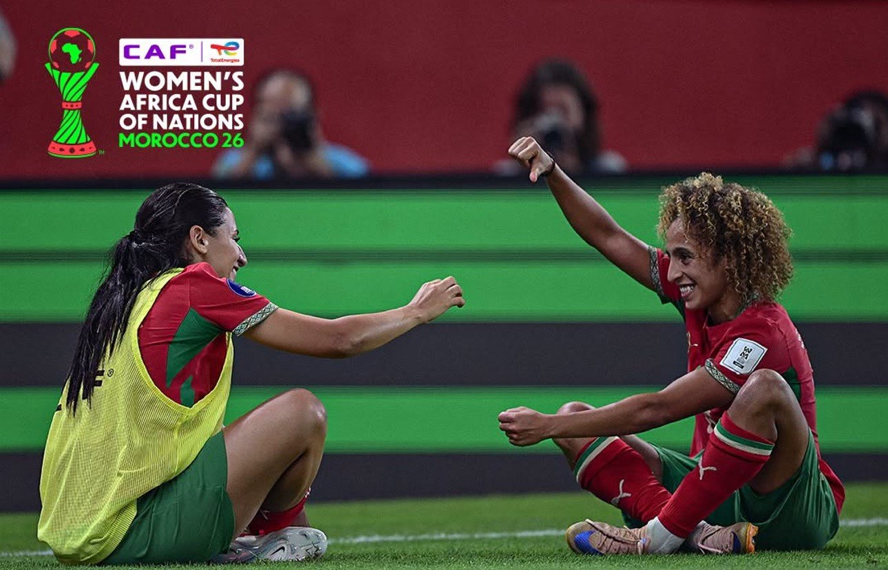 Two female soccer players in red and green celebrate on a green pitch, with the CAF Women's Africa Cup of Nations logo in the corner (Morocco 2026). Two female soccer players in red and green celebrate on a green pitch, with the CAF Women's Africa Cup of Nations logo in the corner (Morocco 2026).
