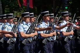 Rows of uniformed soldiers in light blue shirts and black peaked caps march in formation, holding rifles during a parade event. Rows of uniformed soldiers in light blue shirts and black peaked caps march in formation, holding rifles during a parade event.
