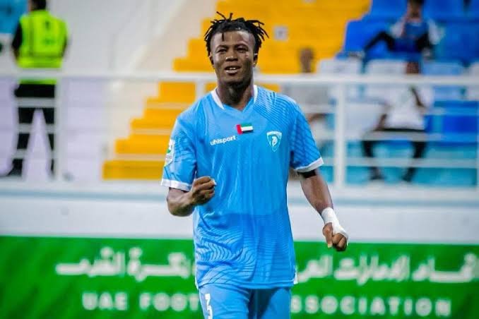 Soccer player in a light blue jersey celebrating on the field, UAE flag on chest, with yellow and blue seats in the stadium background Soccer player in a light blue jersey celebrating on the field, UAE flag on chest, with yellow and blue seats in the stadium background