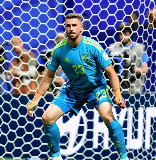 Goalkeeper in a bright blue kit with number 23, crouched in front of the goal during a match.