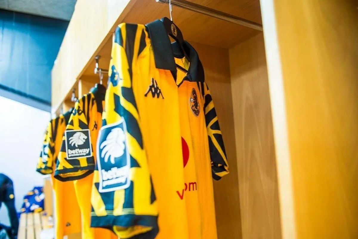Yellow and blue soccer jerseys hanging on hooks in a locker room, with team logos and patches visible on the fronts.