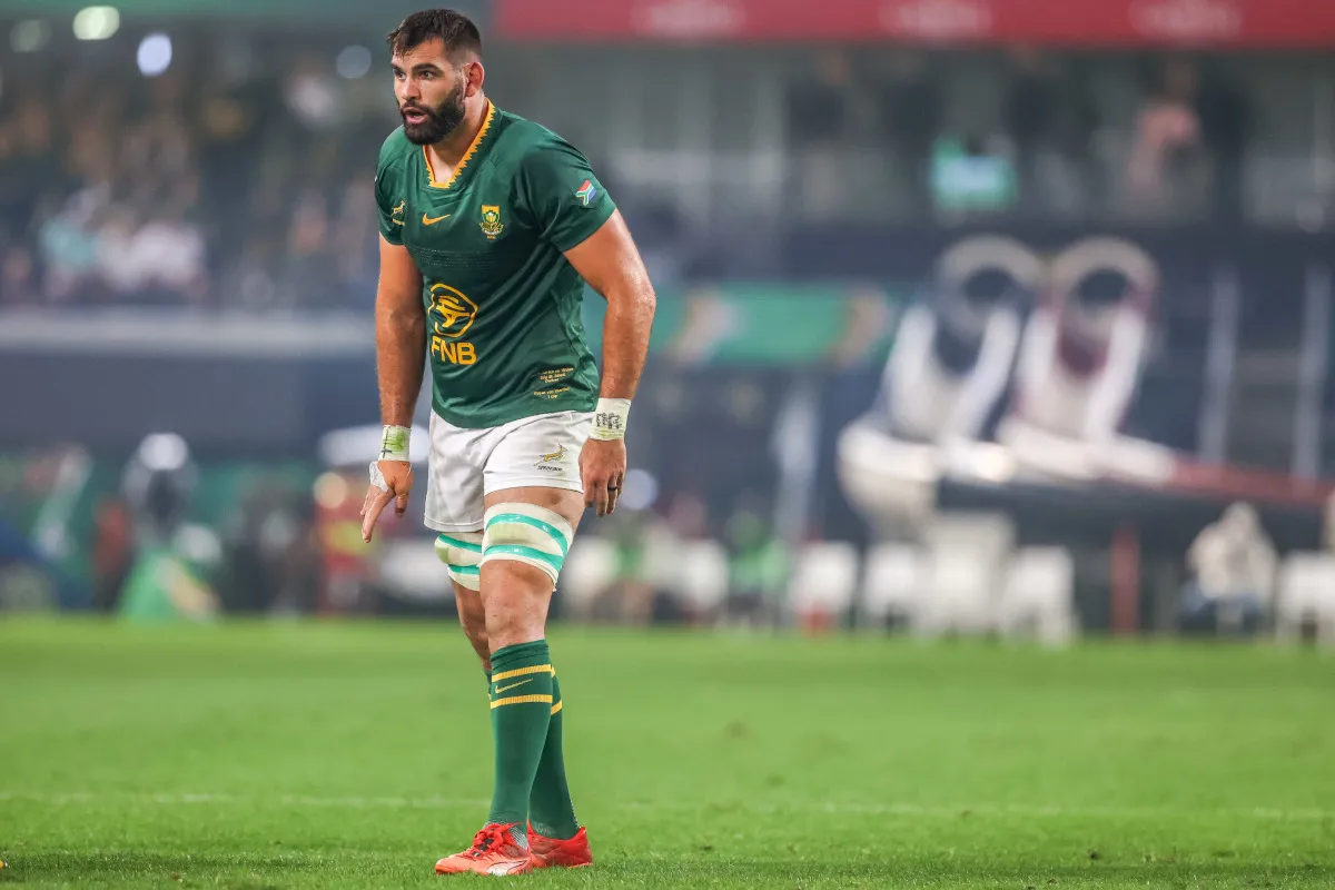 Rugby player in a green South Africa jersey stands on a grass field, white shorts and red cleats visible.