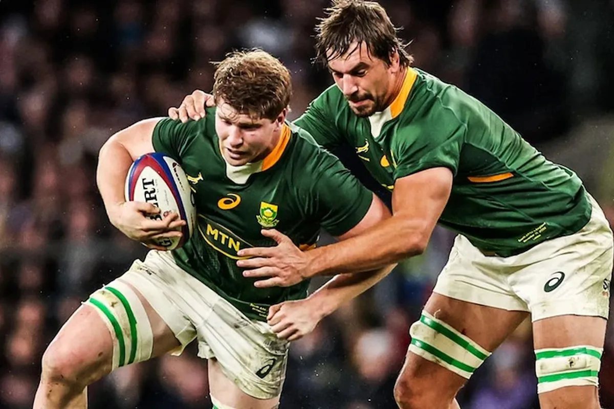 Two rugby players in green and gold jerseys clash for the ball, one holding a rugby ball tightly in front of a crowded stadium.