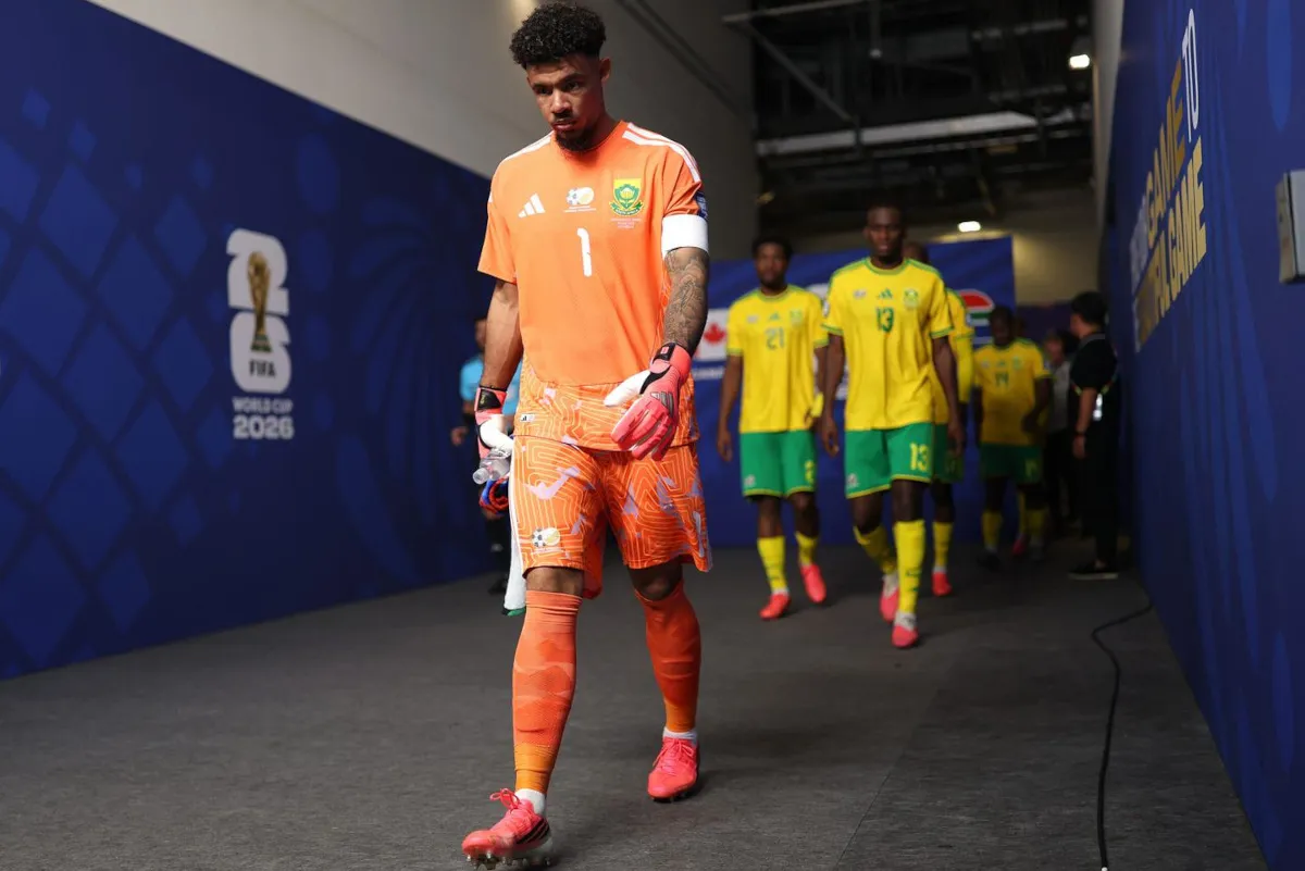 Nigerian goalkeeper in an orange kit and gloves leading a line of yellow-clad teammates through a blue tunnel before a match.