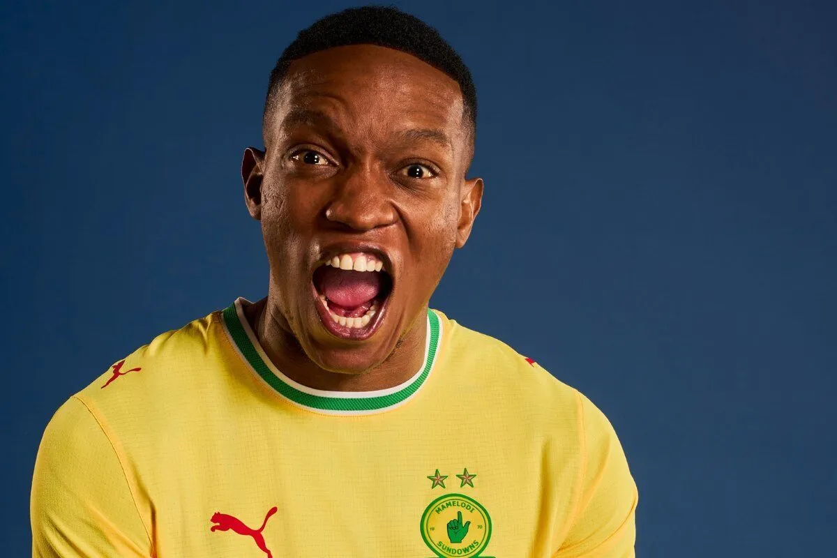 Man in a yellow soccer jersey with green trim shouting with mouth wide open, against a blue background.