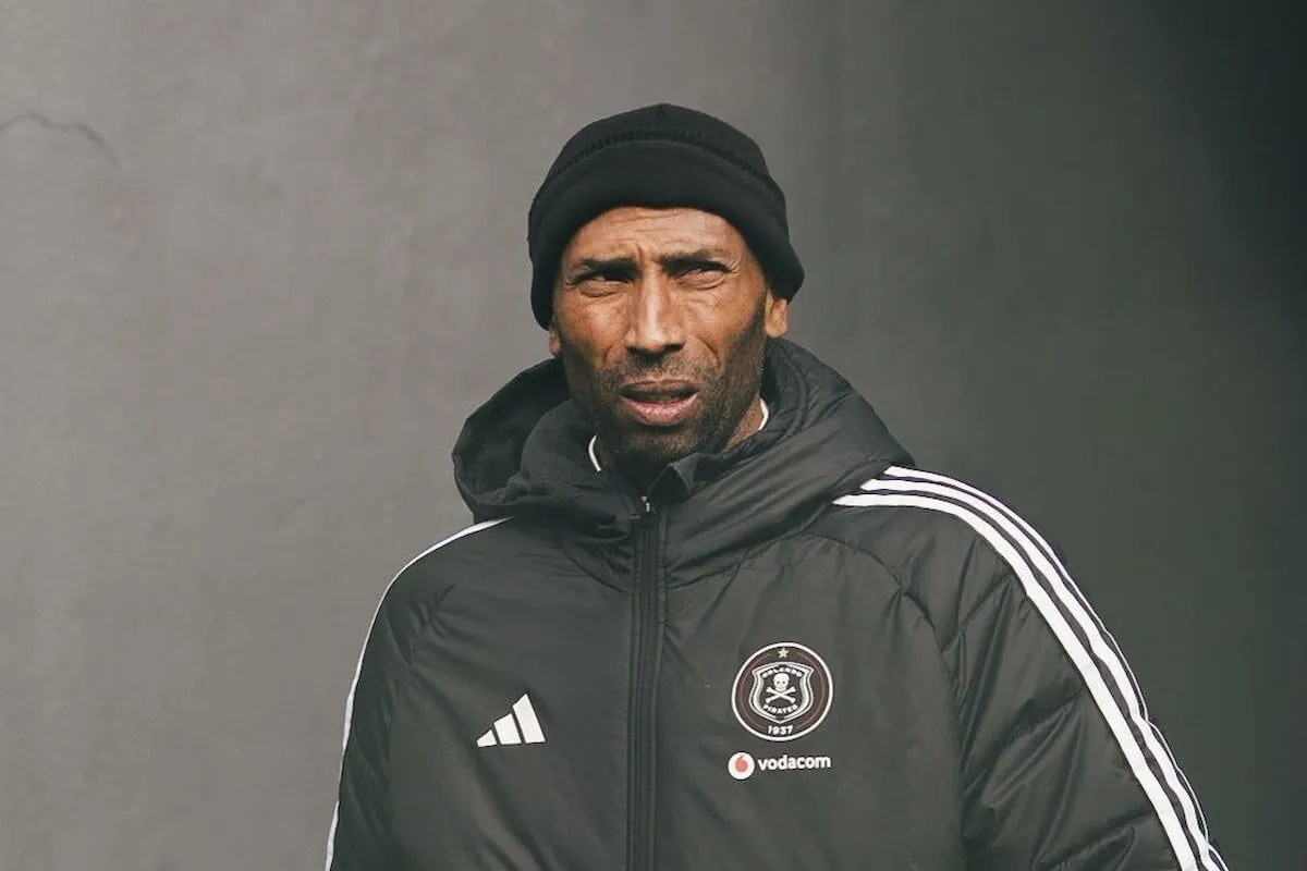 Man in a black beanie and padded jacket with a team crest and Vodacom logo, standing outdoors and looking ahead.