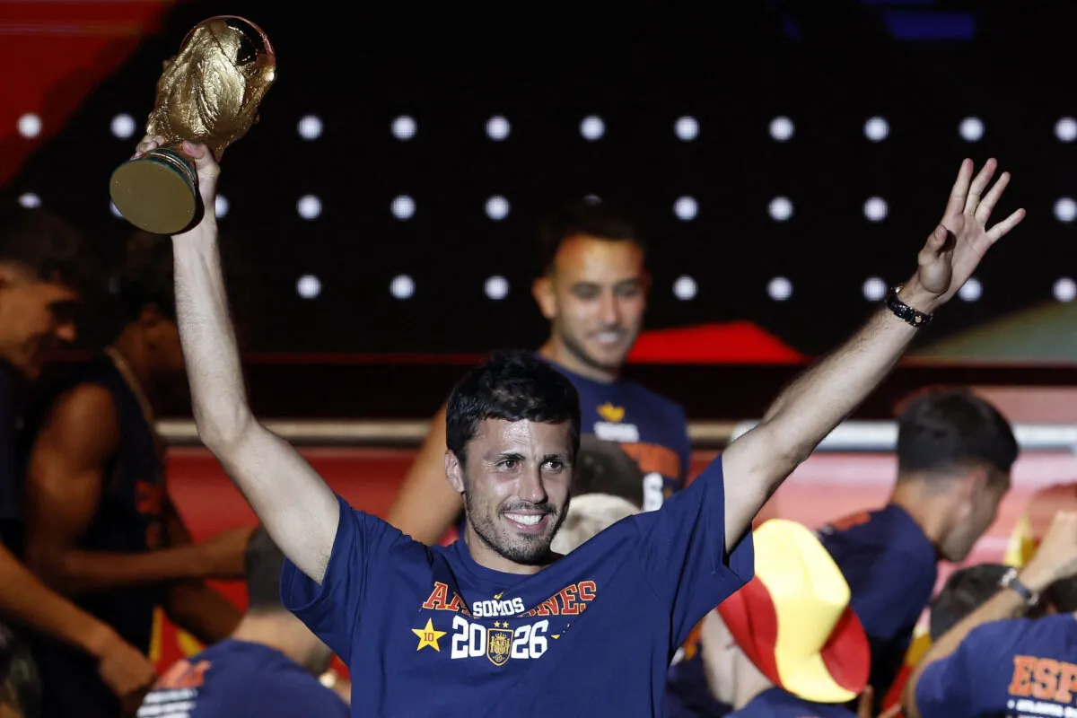 Man in a blue shirt raises a trophy above his head in celebration at a crowded event.