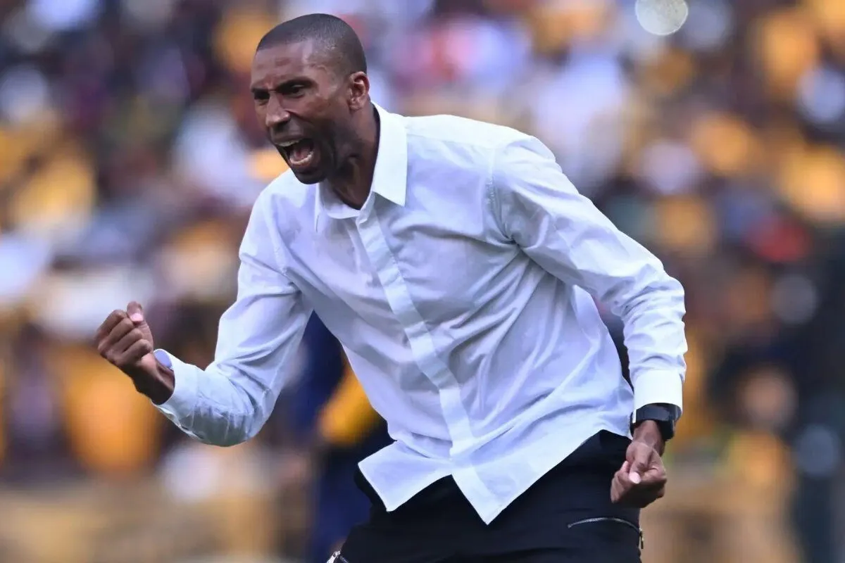 Athlete in a white shirt pumps his fist in celebration on a blurred stadium crowd backdrop