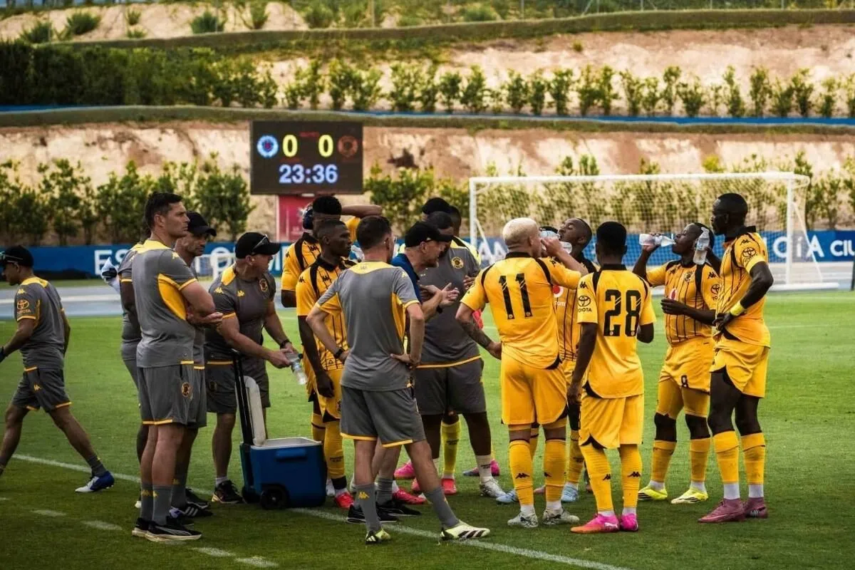 Soccer team in yellow uniforms gathers in a huddle on the field during a match, scoreboard showing 0-0 at 23:36 in the background