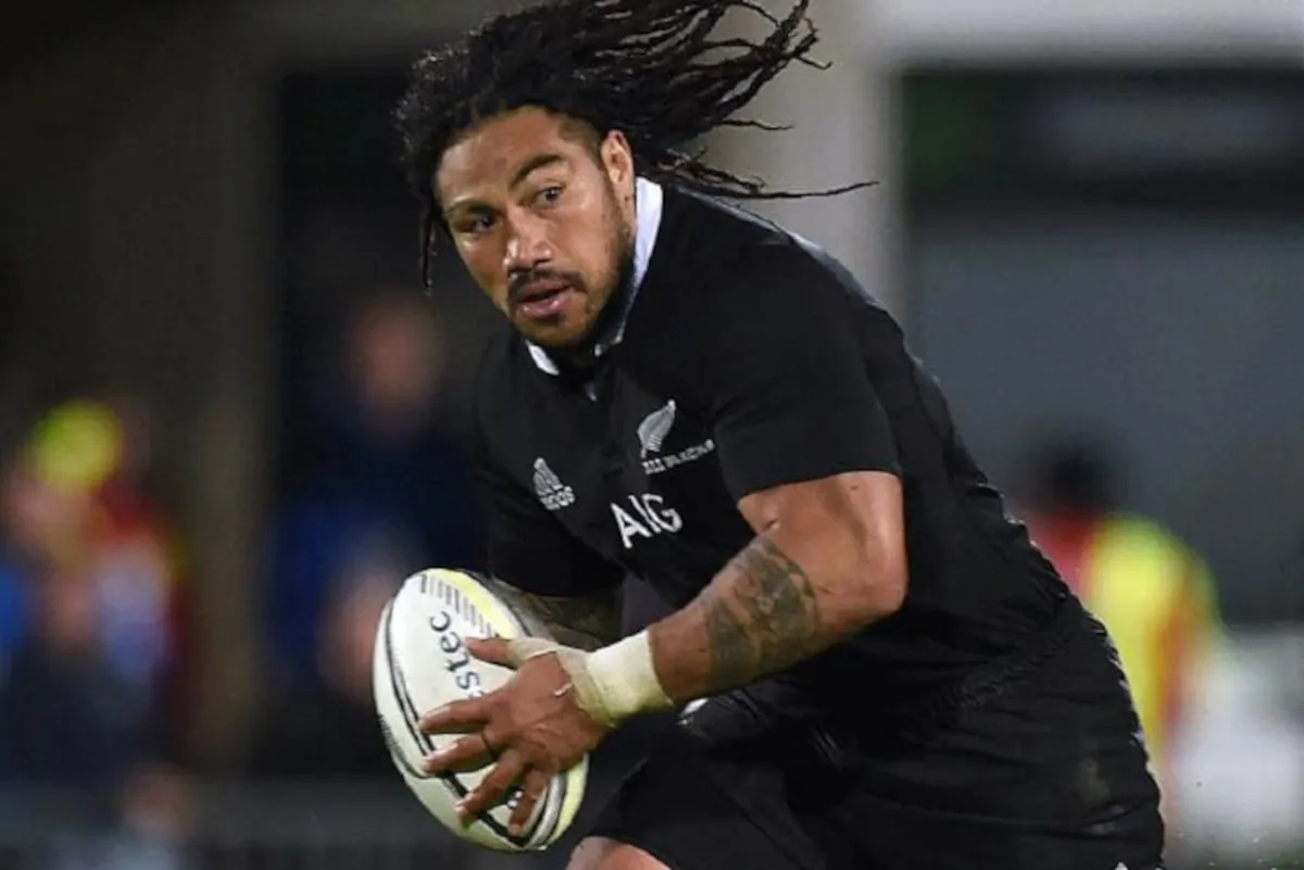 Rugby player in a black kit running with a ball, preparing to pass during a match.