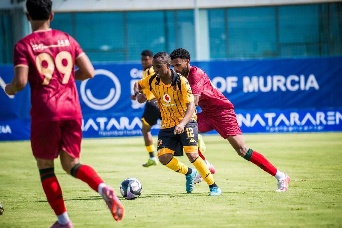 Soccer players chase a ball on a sunny field; a yellow-and-black striped player in front, a red uniform defender close behind, blue goal banner in background. Soccer players chase a ball on a sunny field; a yellow-and-black striped player in front, a red uniform defender close behind, blue goal banner in background.
