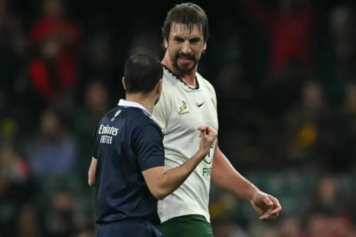 Two soccer players are in a tense moment on the field, one in a white jersey facing a dark-blue kit opponent with a raised fist gesture. Two soccer players are in a tense moment on the field, one in a white jersey facing a dark-blue kit opponent with a raised fist gesture.