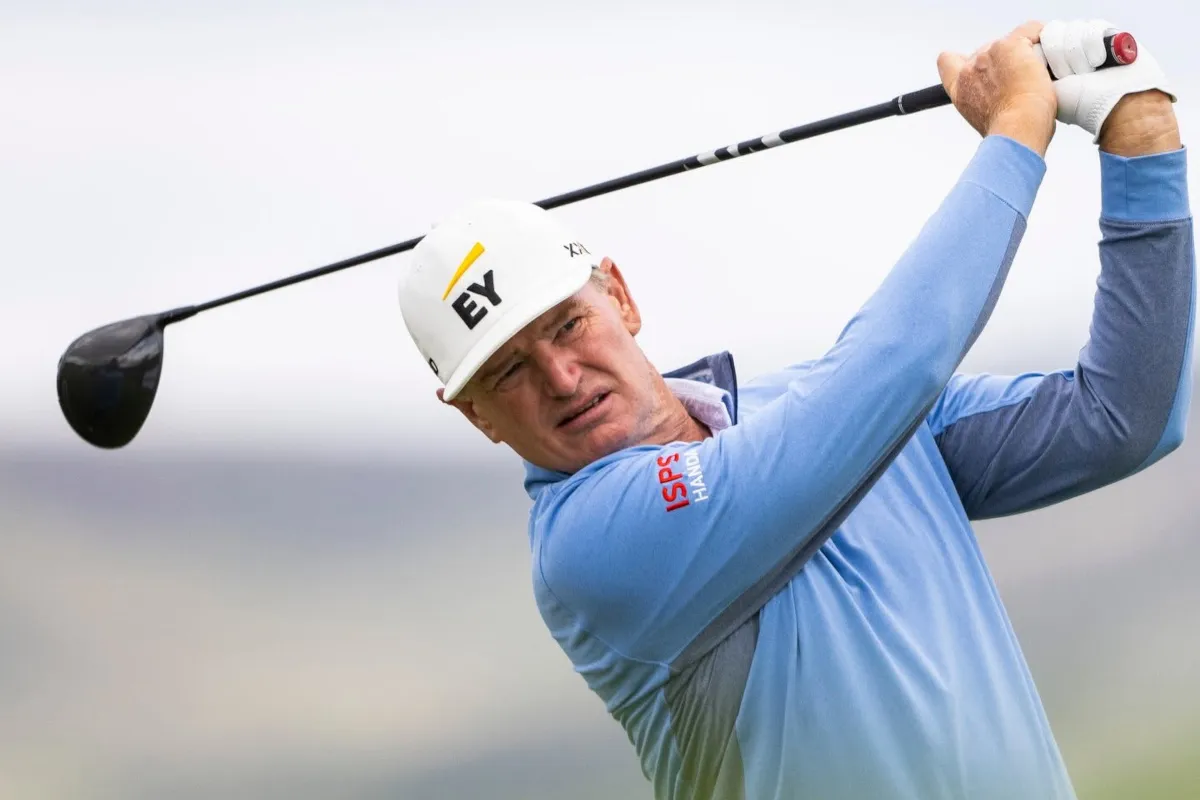 Male golfer in a light blue polo shirt swinging a driver on a golf course, white cap with EY logo visible.