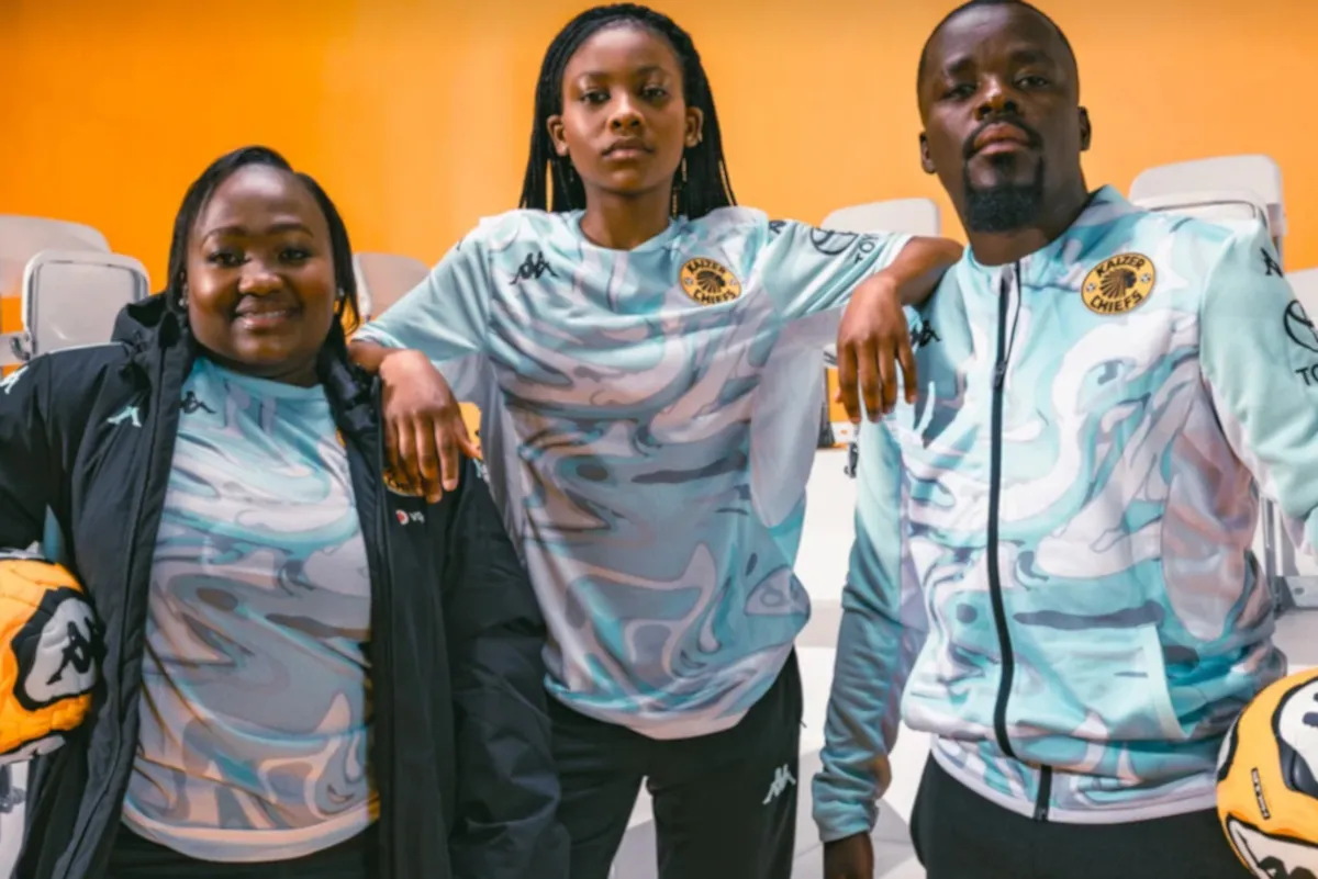 Three athletes in light blue camo tracksuits pose with arms around each other in front of an orange background on a bright set. Three athletes in light blue camo tracksuits pose with arms around each other in front of an orange background on a bright set.