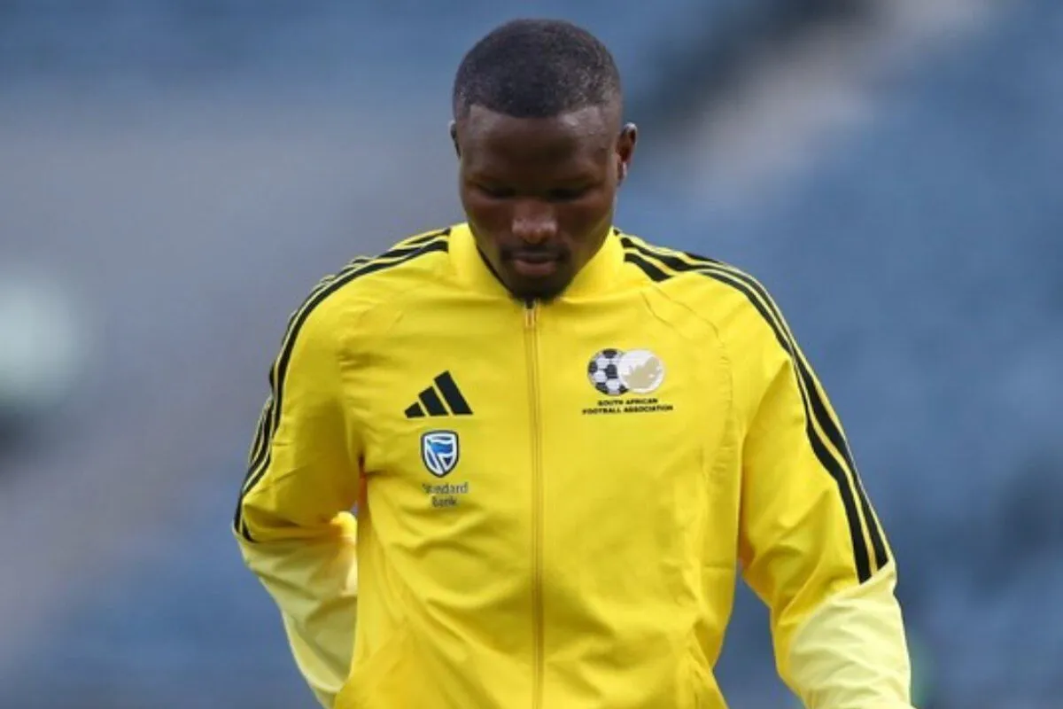Soccer player in a bright yellow jacket with black stripes, looking down during training on a field