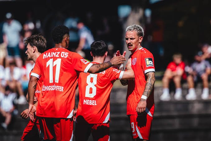 Three soccer players in red uniforms celebrate on the field with a high-five, numbers 11 and 8 visible, blurred spectators in the stands. Three soccer players in red uniforms celebrate on the field with a high-five, numbers 11 and 8 visible, blurred spectators in the stands.