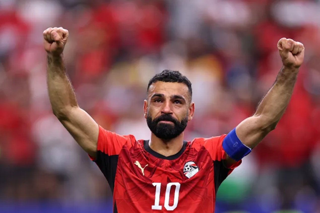 Soccer player in a red jersey with number 10 raises both fists in celebration on the field. Soccer player in a red jersey with number 10 raises both fists in celebration on the field.