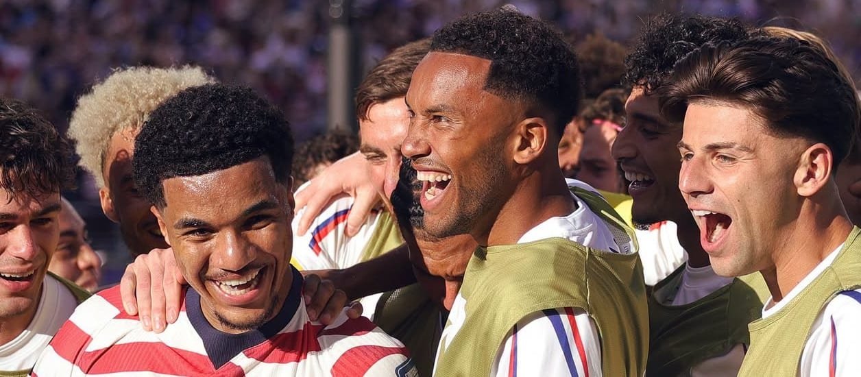 A group of soccer players celebrate together on the field, smiling and embracing each other.