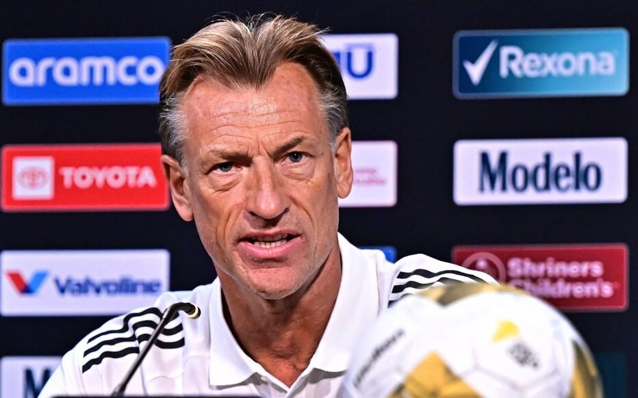 Man speaking at a sports press conference, microphone in front, sponsor logos on the backdrop behind him. Man speaking at a sports press conference, microphone in front, sponsor logos on the backdrop behind him.