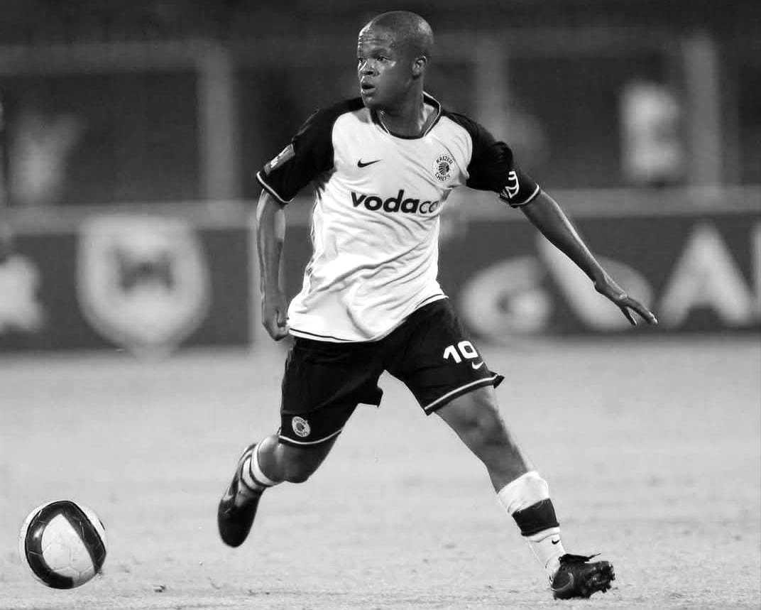 Male soccer player in white and black kit dribbling the ball on the field.