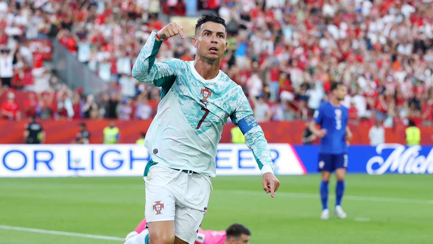 Soccer player in a light-blue Portugal jersey celebrates a goal on a crowded stadium field across green pitch. Soccer player in a light-blue Portugal jersey celebrates a goal on a crowded stadium field across green pitch.