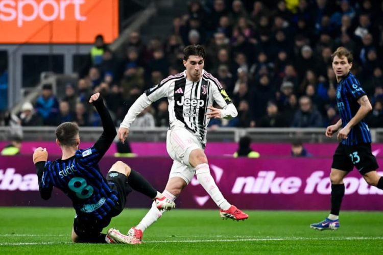 Juventus player in white-black stripes dribbles the ball while a blue-jersey opponent slides in for a tackle on a green pitch, with spectators in the stands. Juventus player in white-black stripes dribbles the ball while a blue-jersey opponent slides in for a tackle on a green pitch, with spectators in the stands.