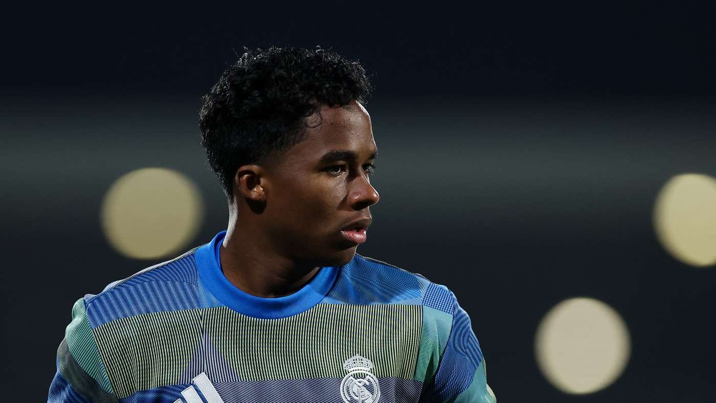 Soccer player in Real Madrid training kit looking to the right with blurred stadium lights behind.