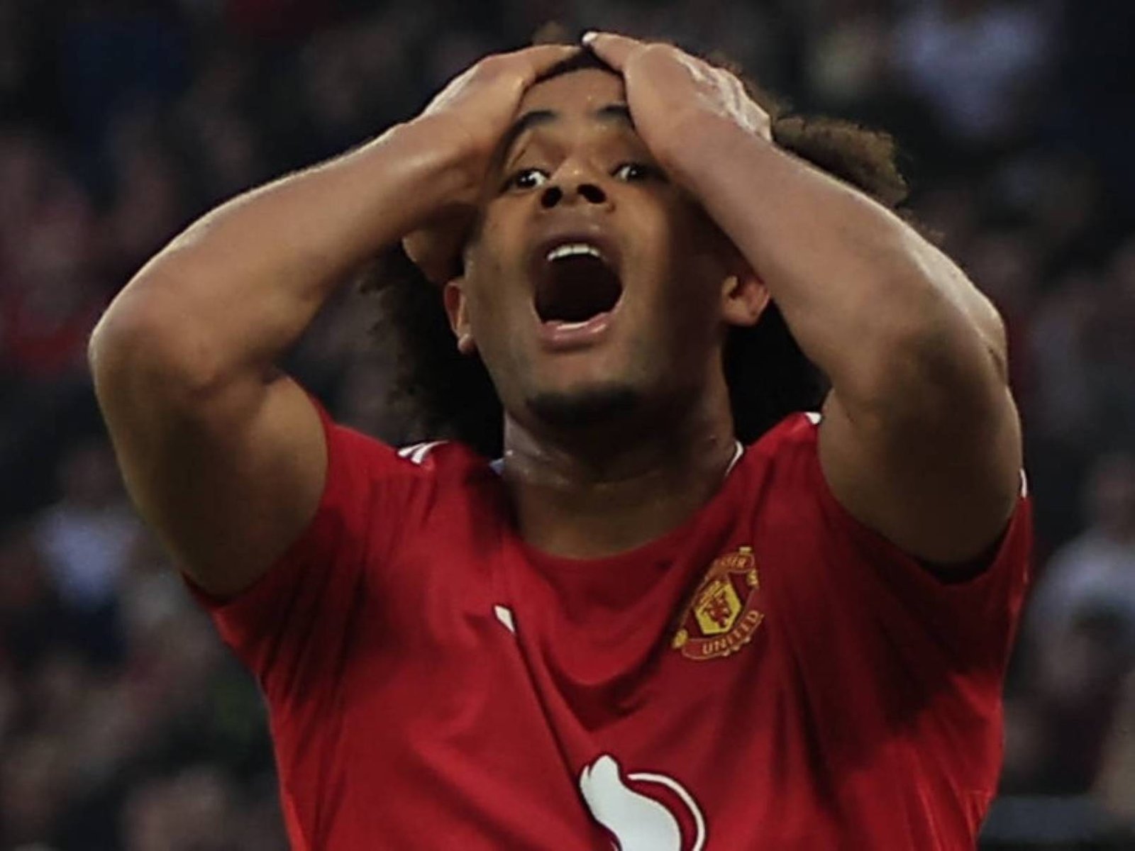Footballer in a red Manchester United jersey holding his head in frustration on the field at a match.