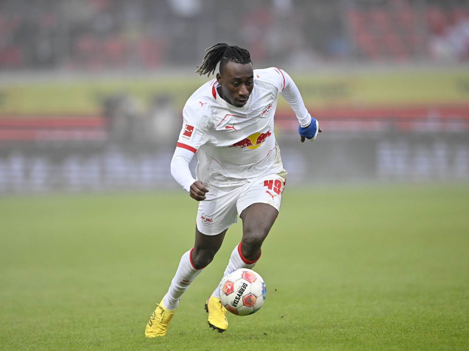Soccer player in a white jersey dribbling a ball on a green field during a match.