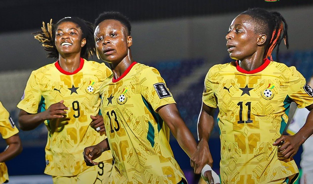 Three female soccer players in yellow jerseys sprint on a stadium pitch during a match. Three female soccer players in yellow jerseys sprint on a stadium pitch during a match.