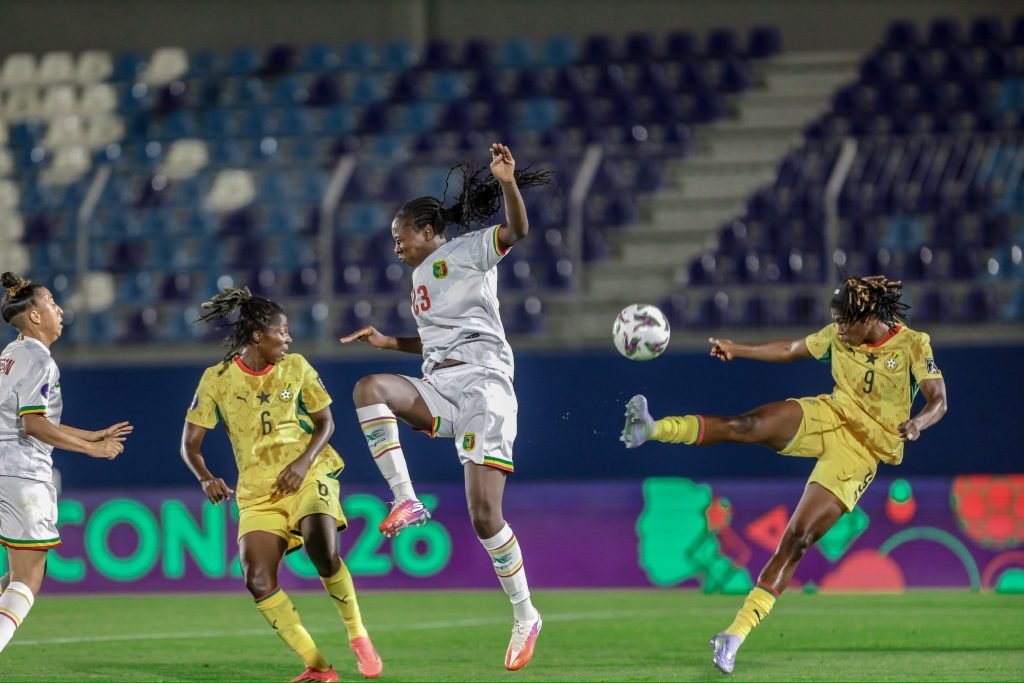 Soccer players in white and yellow kits contest a ball in mid-air on a well-lit stadium field. Soccer players in white and yellow kits contest a ball in mid-air on a well-lit stadium field.