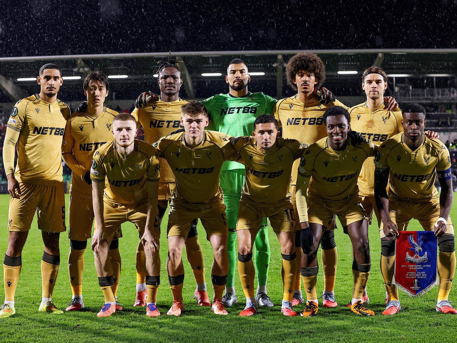 Soccer team in gold jerseys posing for a group photo on the field, goalkeeper in green at center back row. Soccer team in gold jerseys posing for a group photo on the field, goalkeeper in green at center back row.
