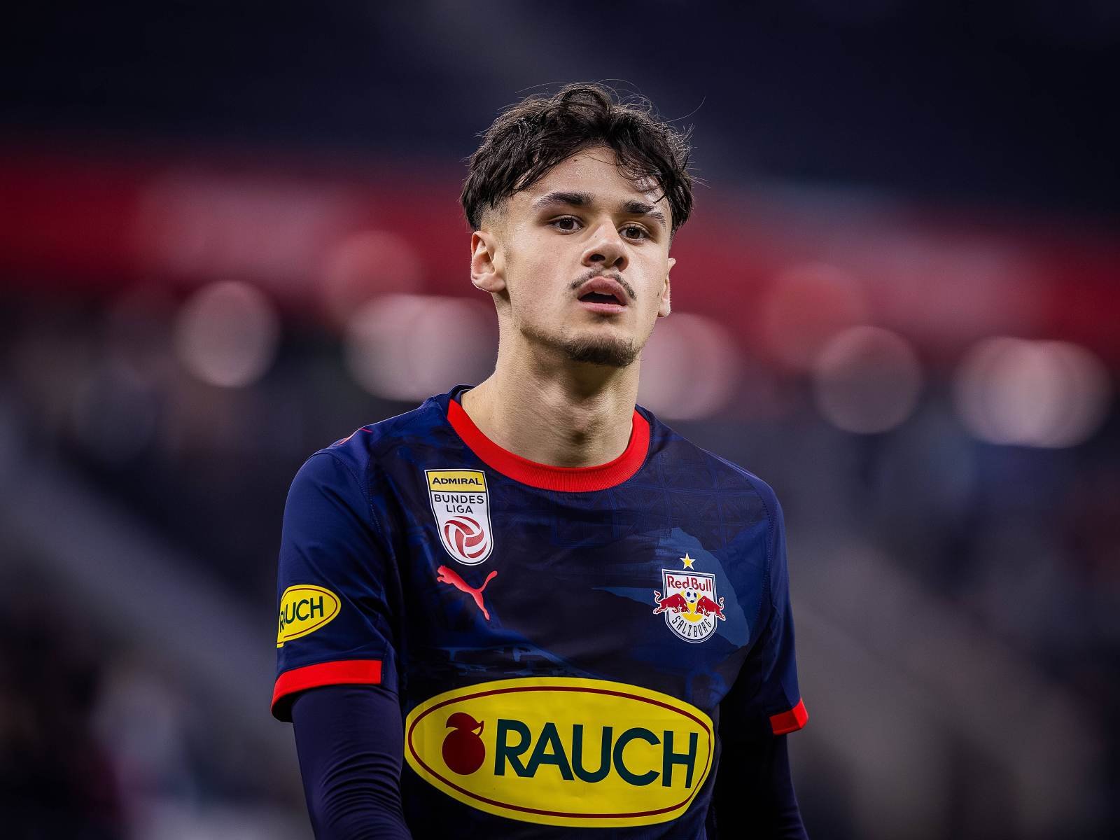 Portrait of a Red Bull Salzburg footballer in a navy kit with sponsor patches, looking ahead on the field. Portrait of a Red Bull Salzburg footballer in a navy kit with sponsor patches, looking ahead on the field.