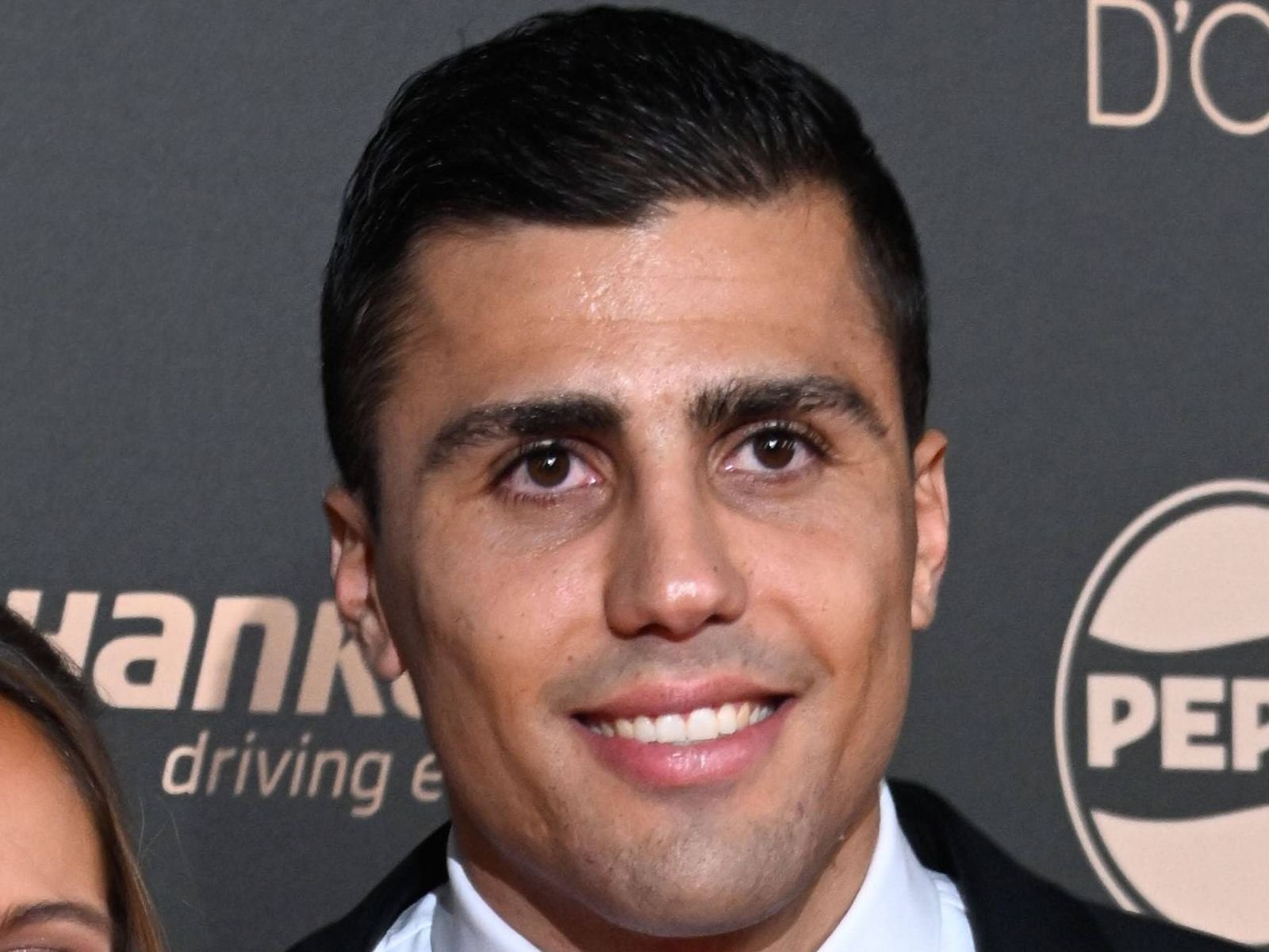 Close-up of a man in a dark suit smiling at the camera at a media backdrop.