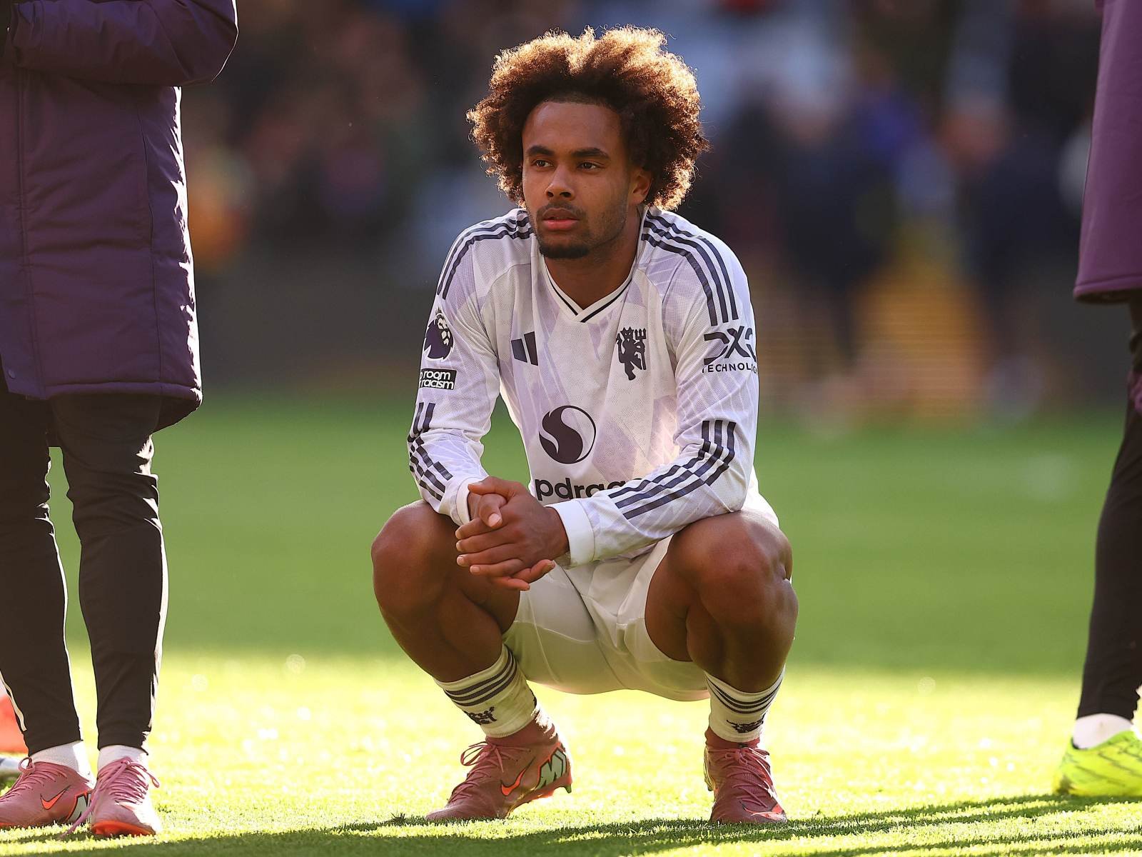 Soccer player crouching on a sunny grass field during warm-up, wearing a white jersey and pink cleats.