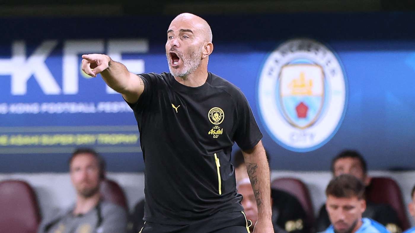 Bald football manager shouting and pointing from the touchline during a match.
