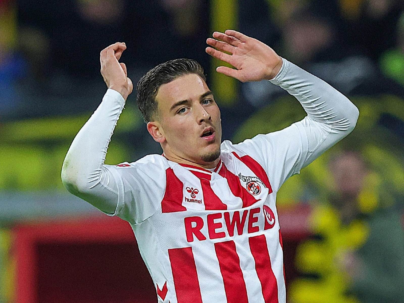 Soccer player in white and red striped jersey raising arms in celebration