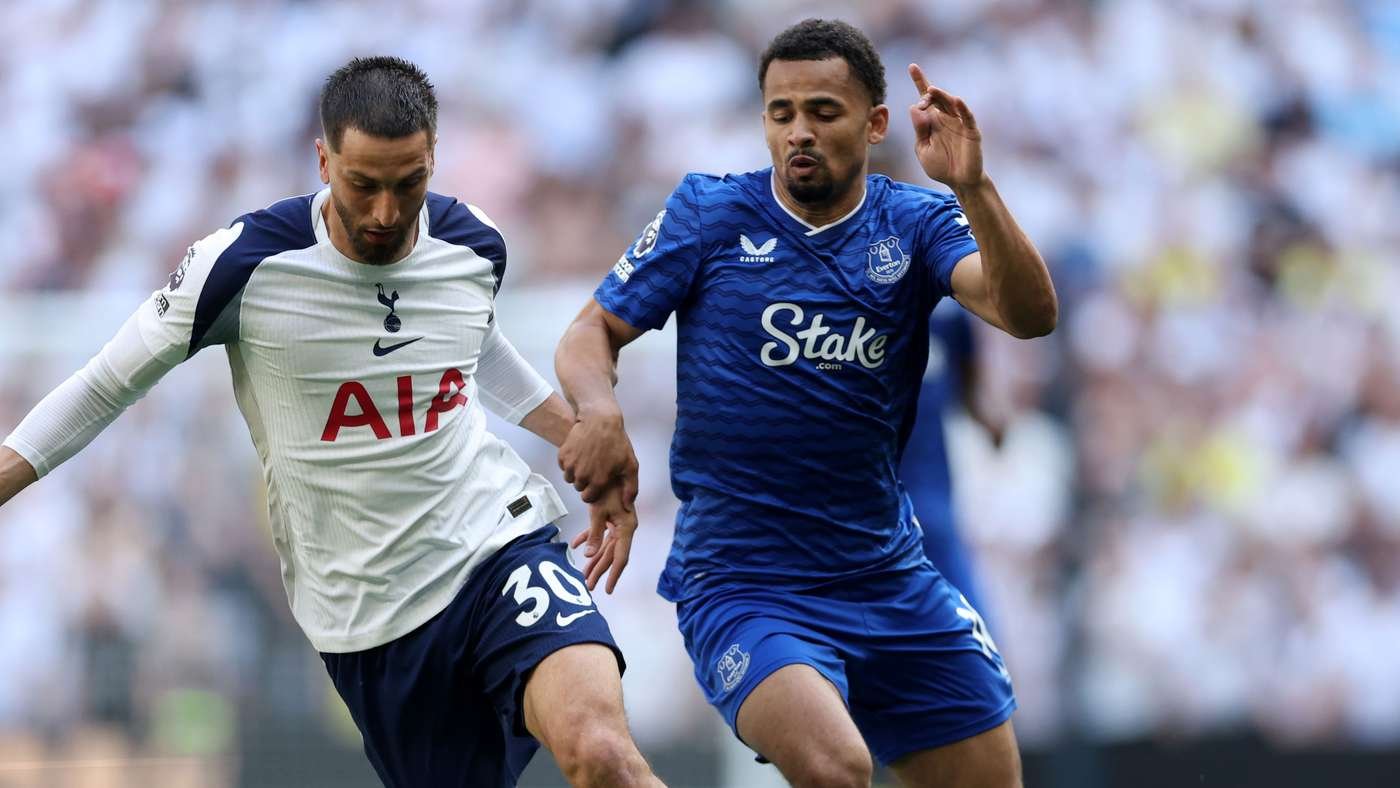 Two soccer players compete for the ball during a match; one in a white Tottenham jersey and the other in a blue Everton jersey.
